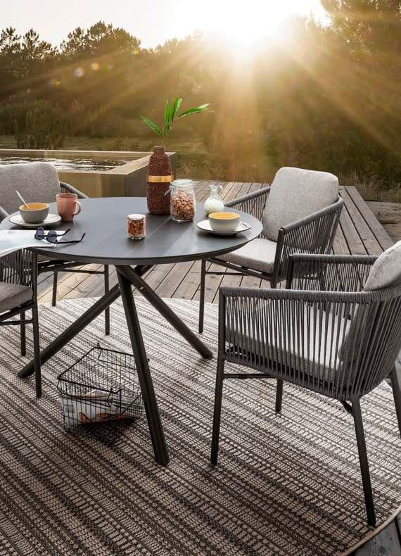 Outdoor-Tisch mit Frühstücksutensilien, umgeben von Stühlen auf einer Terrasse bei Sonnenaufgang.