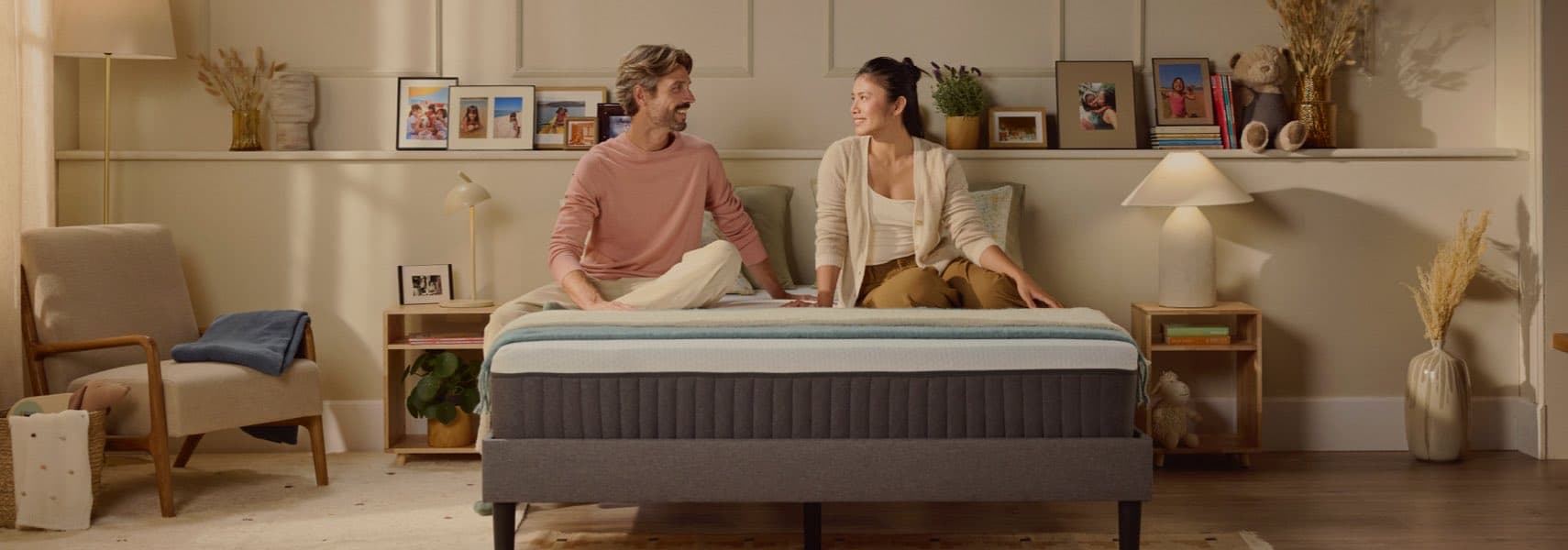 Zwei Personen sitzen auf einem Bett in einem gemütlichen, dekorierten Zimmer mit Fotos und Lampen.