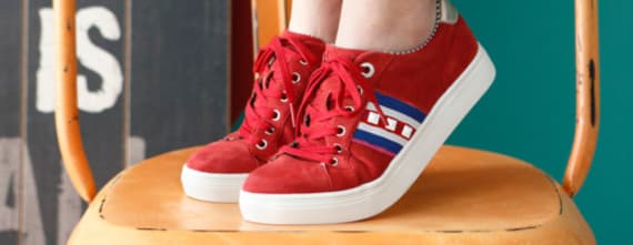 Rote Sneakers mit blauen und weißen Streifen auf einem Hocker.