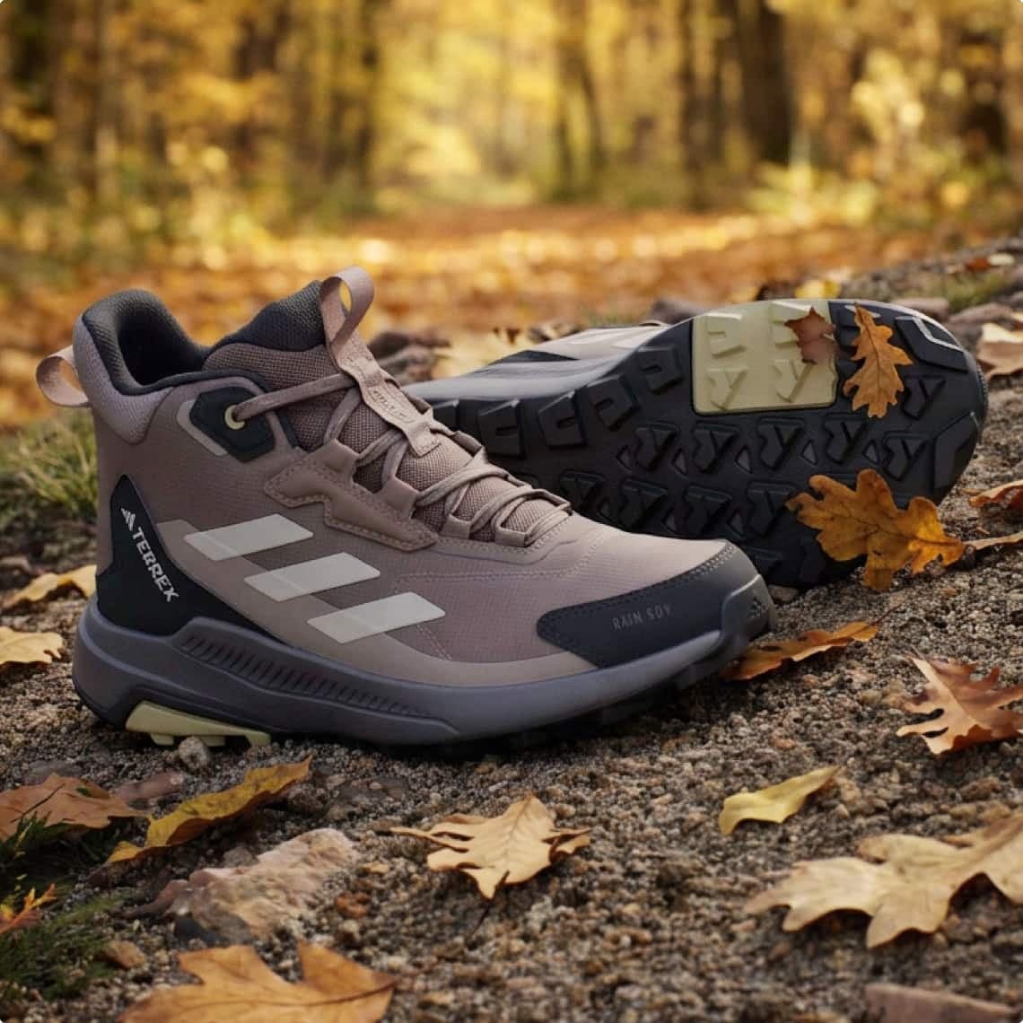 Outdoor-Sneakerpaar mit Profilsohle auf herbstlichem Waldweg, ein Schuh stehend, der andere liegend mit Laub auf der Sohle