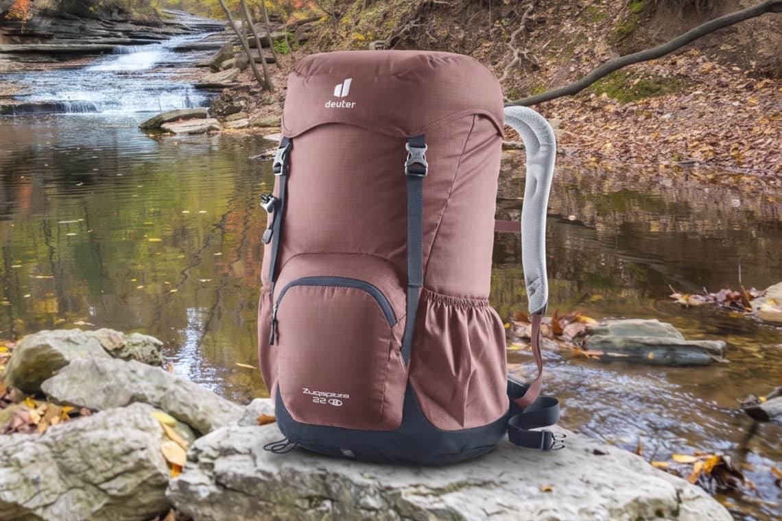 Wanderrucksack von Deuter steht auf Felsen am Bachlauf mit kleinem Wasserfall und herbstlichem Wald im Hintergrund