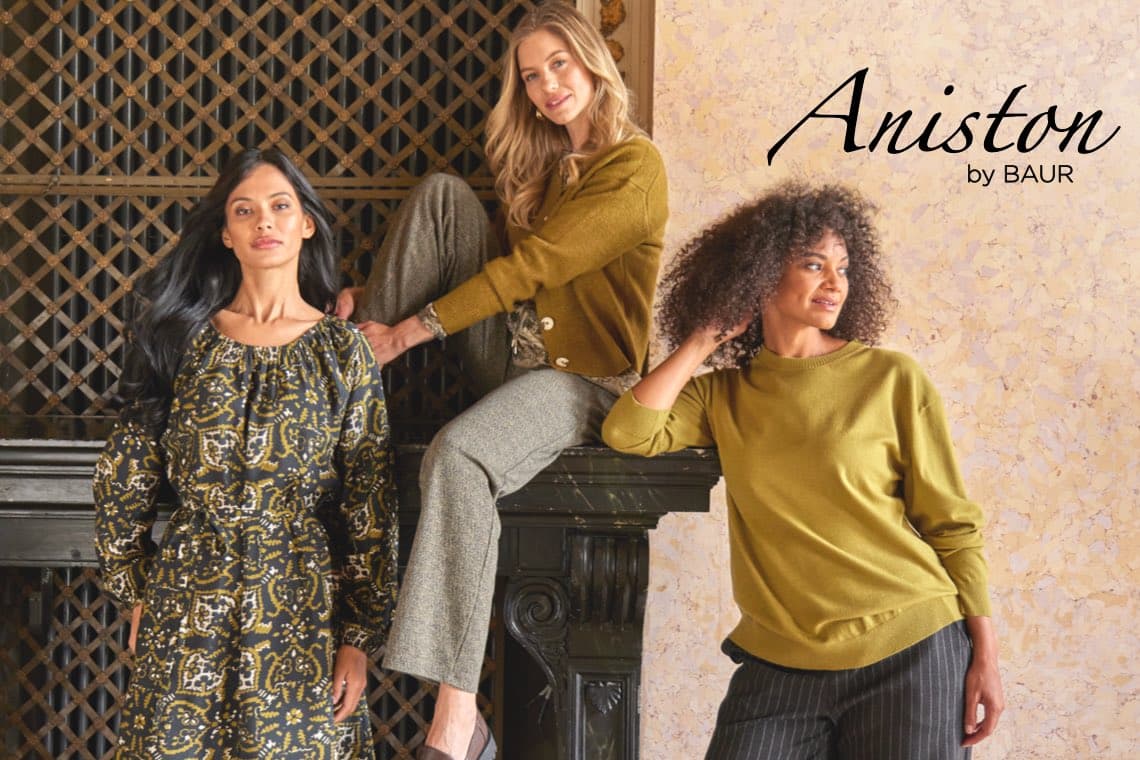 Aniston by BAUR – drei Frauen posieren in herbstlicher Mode vor Kamin und gemusterter Wand