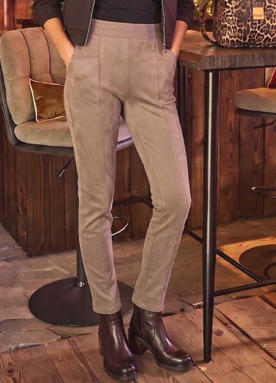Person in beiger schmaler Hose und dunklen Stiefeletten steht an einer Bar mit Hocker und Leoparden-Tasche