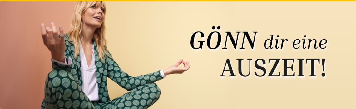 GÖNN dir eine AUSZEIT! – Frau in grüner gemustertem Hosenanzug sitzt im Meditationspose vor farbigem Hintergrund