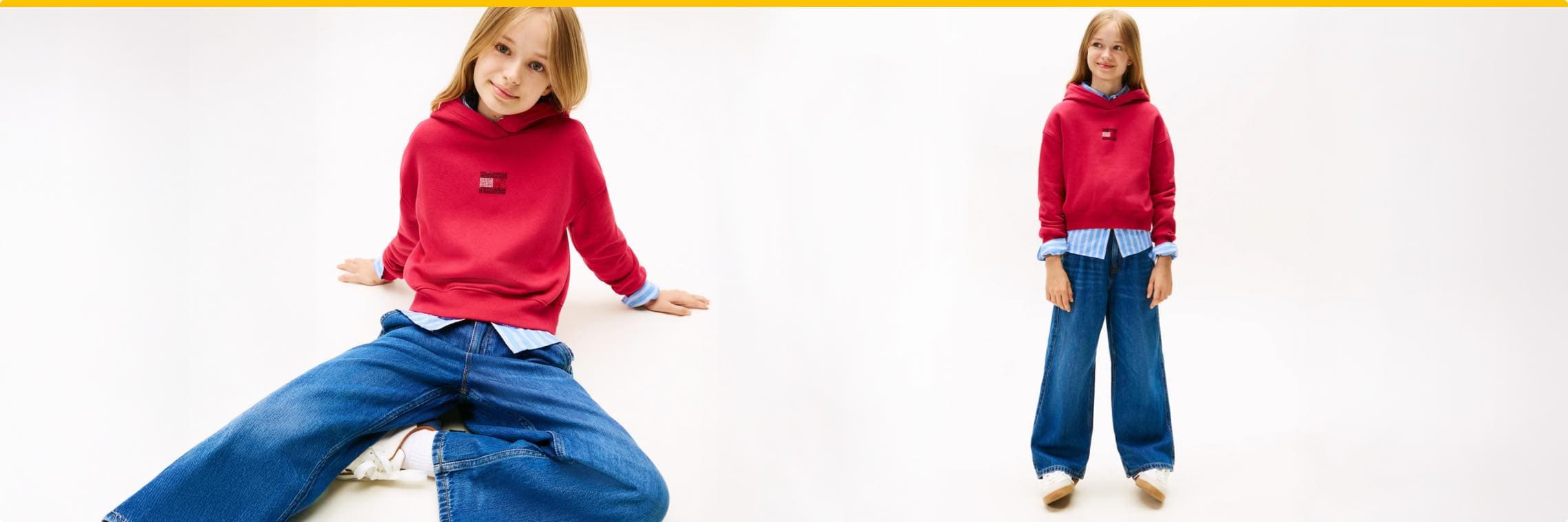 Kind in rotem Hoodie mit blauem Hemd darunter und weiten Jeans, sitzt und steht vor weißem Hintergrund.