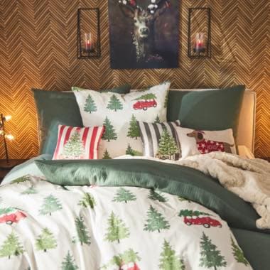 Weihnachtlich dekoriertes Bett mit Tannenbaum- und Autodesign, Kissen und Decke, im Hintergrund ein Hirschbild und Kerzenhalter