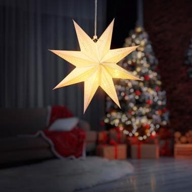 Leuchtender Sternanhänger vor einem festlich geschmückten Weihnachtsbaum, im Hintergrund ein Sofa mit roter Decke und Geschenke.