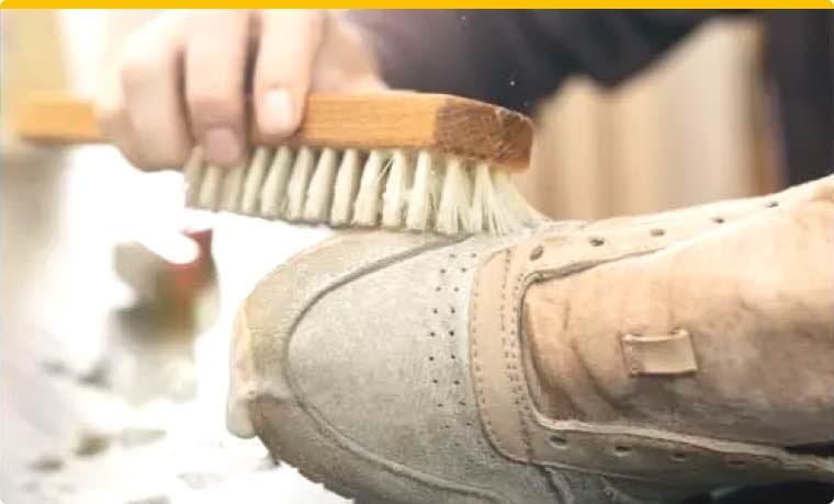 Hand reinigt grauen Schuh mit einer Bürste, Nahaufnahme von der Seite