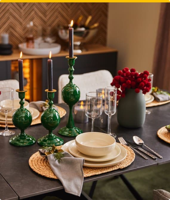 Festlich gedeckter Weihnachtstisch mit dunkelgrünen Kerzenhaltern und hellem Geschirr.