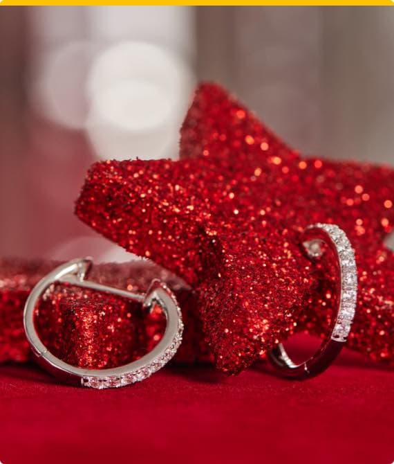 Zwei silberne Creolen mit Glitzersteinen vor rotem glitzernden Stern auf rotem Hintergrund