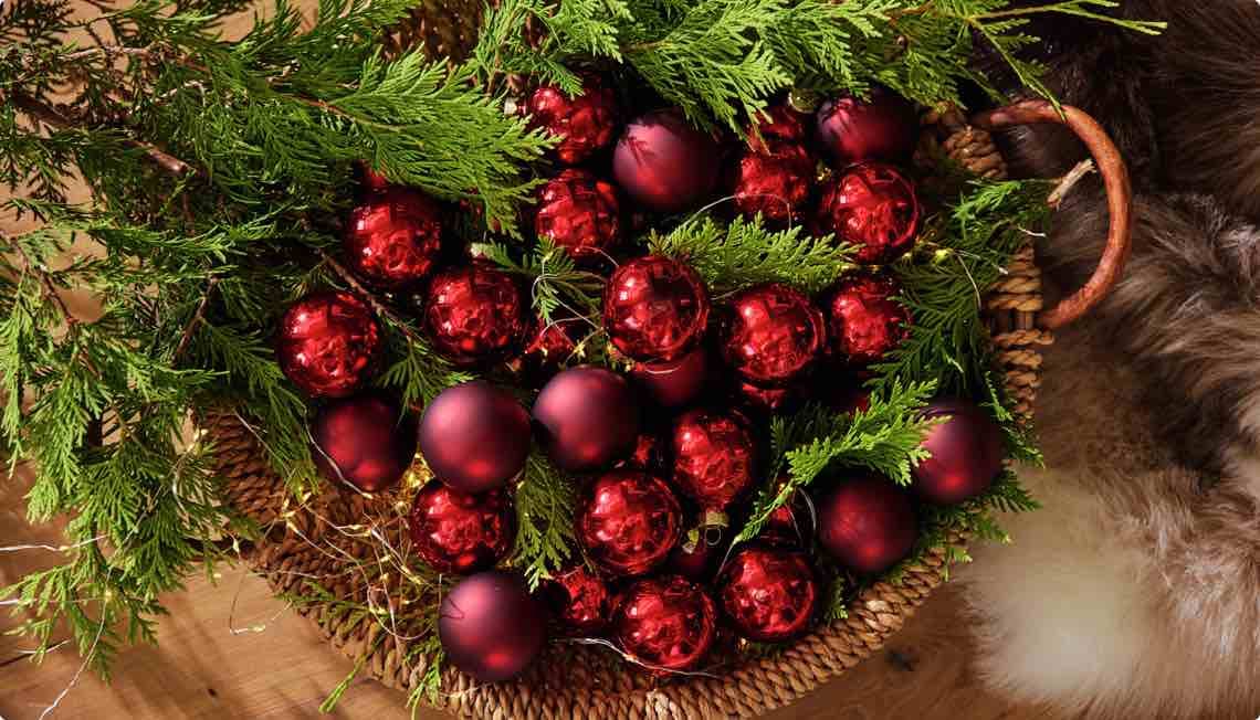 Rote Weihnachtskugeln und grüne Zweige in einem Korb auf einem Holztisch