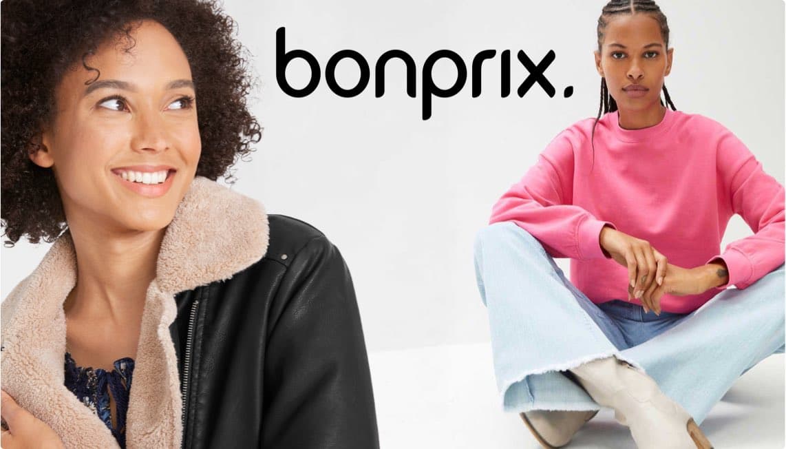 bonprix – Frau in schwarzer Jacke mit Fellkragen, daneben Frau in rosa Pullover und hellblauer Jeans sitzt auf weißem Boden.