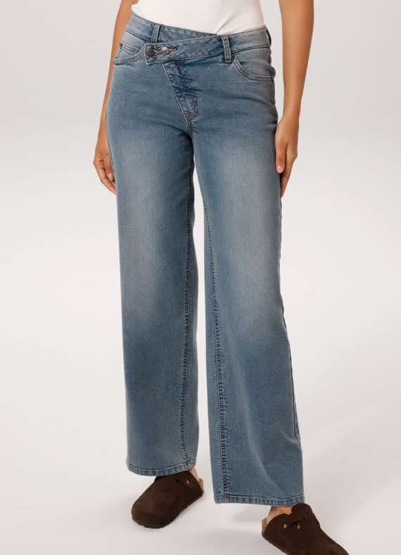 Frau trägt weit geschnittene Jeans mit asymmetrischem Bund und braunen Schuhen.