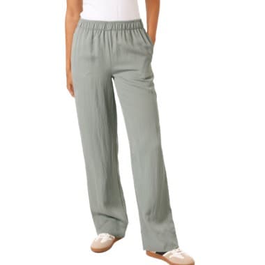 Frau trägt weite, graue Hose mit elastischem Bund und weißem Oberteil, Hände in den Taschen.