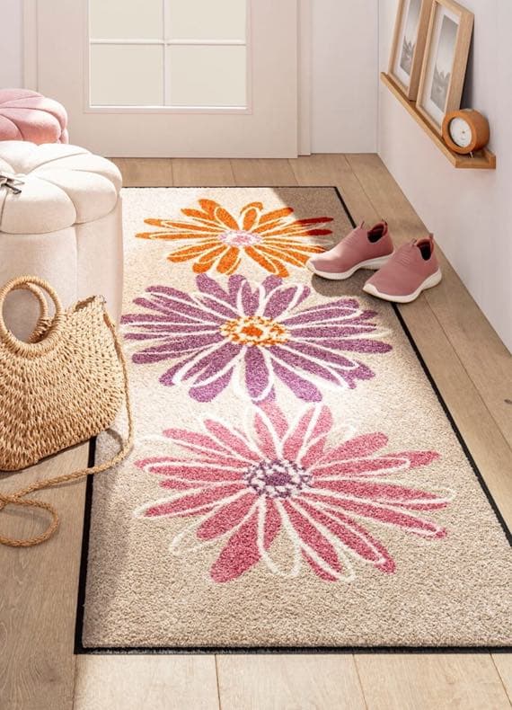 Blumenvorleger mit rosa, lila und orange Blumen auf beige. Rosa Schuhe und Strohtasche im Eingangsbereich.