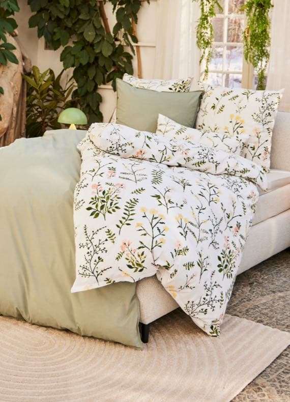 Bett mit Blumenbettwäsche und grüner Decke, dekoriert mit Pflanzen in gemütlicher Atmosphäre.