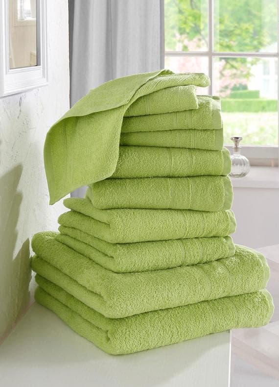 Ein Stapel grüner Handtücher in einem hellen Raum vor einem Fenster.