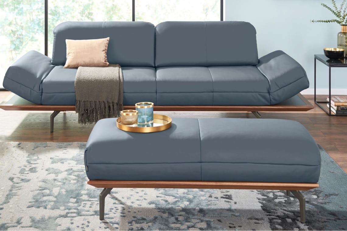 Blaue Couch und Ottomane, beide mit Holzrahmen. Couch mit Kissen und Decke, Ottomane mit goldfarbenem Tablett und Kerzen.