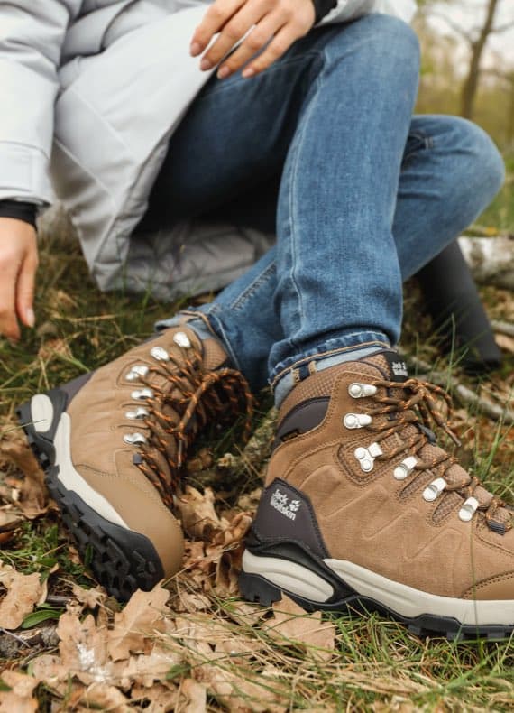 Person sitzt im Wald und trägt braune Wanderschuhe mit blauen Jeans.