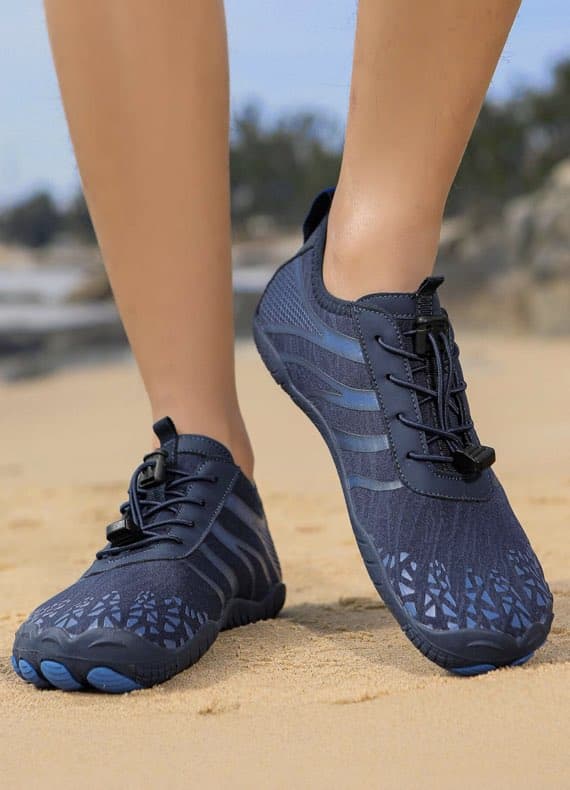 Person trägt dunkelblaue Wasserschuhe am Strand.