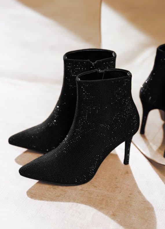 Schwarze Stiefeletten mit glitzernden Details und spitzen Absätzen auf hellem Untergrund.