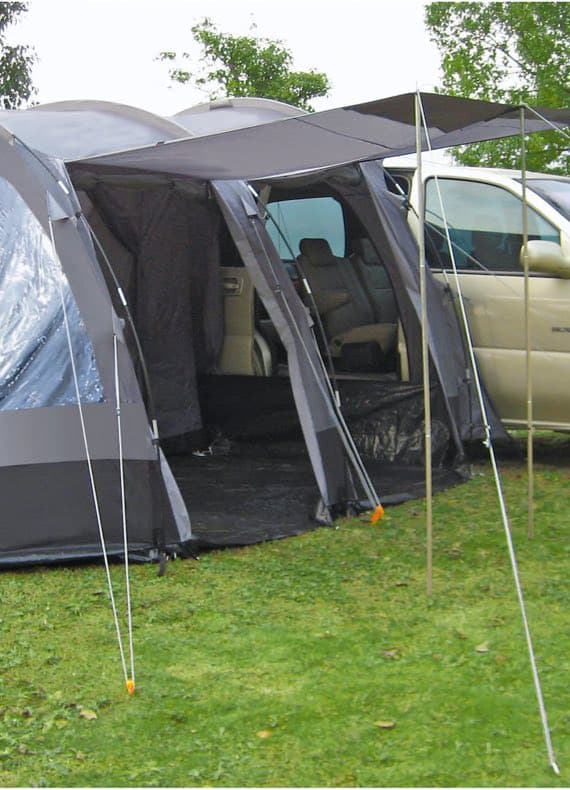 Großes graues Zelt mit Vordach, verbunden mit einem geparkten Auto, auf einer grünen Wiese.