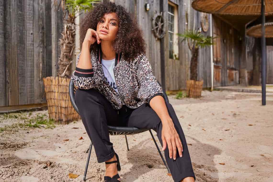 Modisch gekleidete Dame sitzt lässig auf einem Stuhl im Freien und blickt in die Kamera.