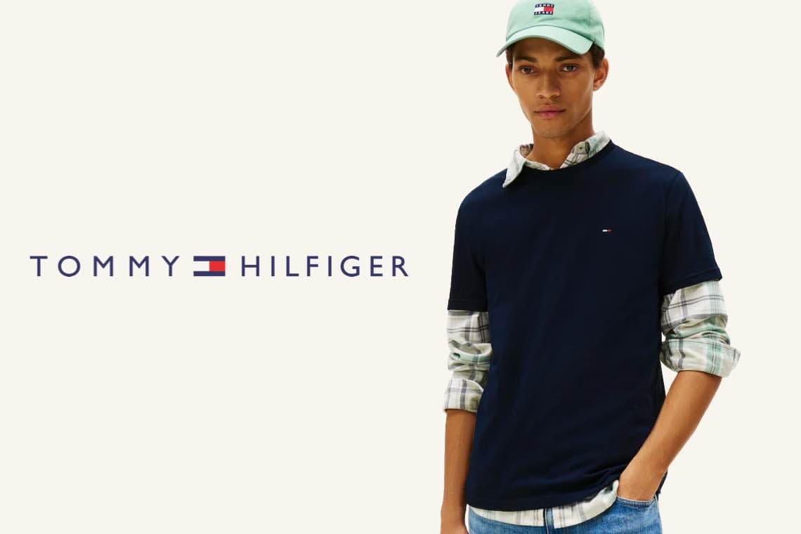 TOMMY HILFIGER – Mann trägt dunkelblaues Shirt über kariertem Hemd und hellgrüne Kappe