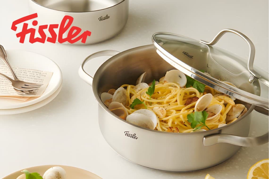 Fissler – Topf mit geöffnetem Deckel, gefüllt mit Spaghetti, Muscheln und Kräutern auf heller Arbeitsfläche