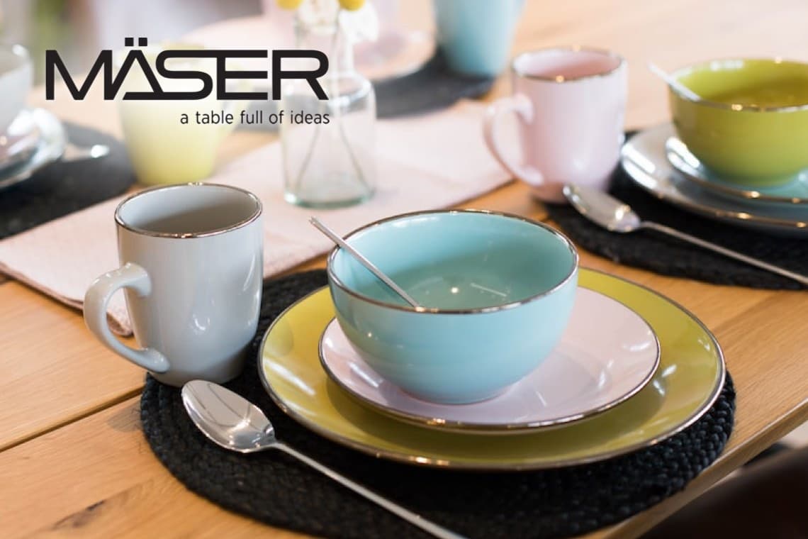 MÄSER – a table full of ideas – gedeckter Holztisch mit buntem Tellerset, Schalen, Tassen und Besteck auf Platzsets
