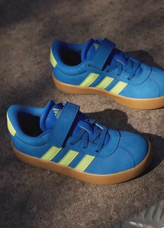 Blaue Kinderturnschuhe mit gelben Streifen und Klettverschluss liegen nebeneinander auf grauem Boden