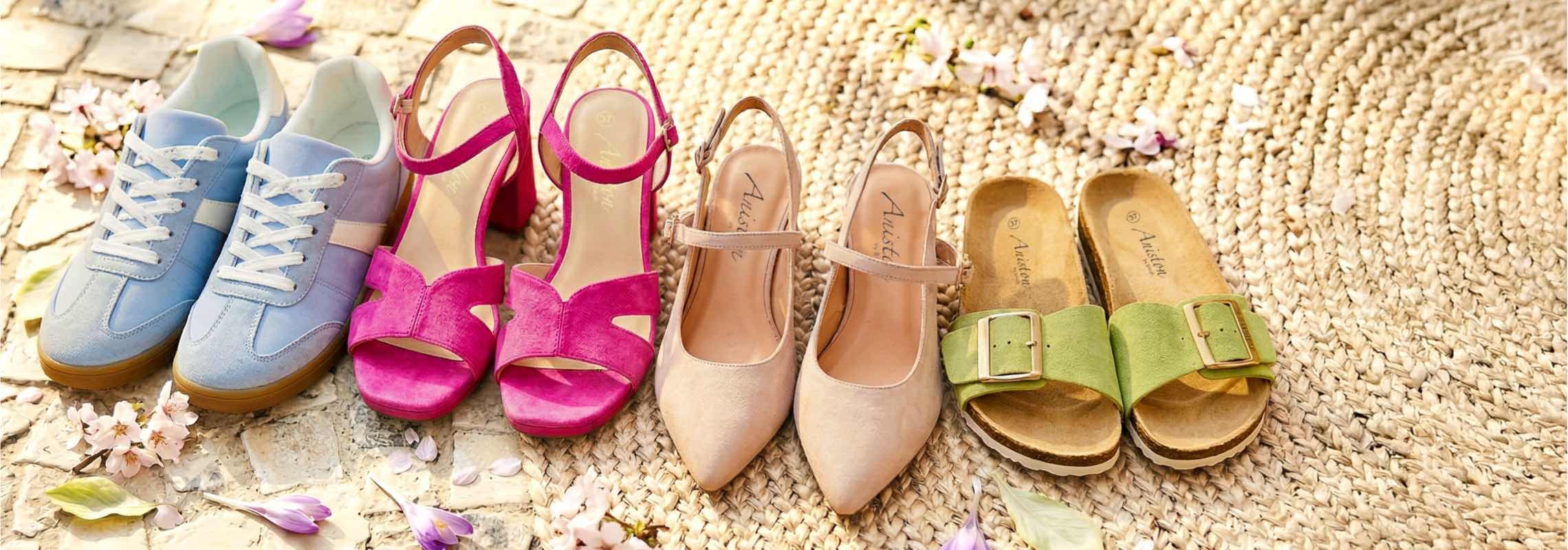 Vier Paar Sommerschuhe auf Bastteppich: blaue Sneaker, pinke Sandaletten, nudefarbene Pumps und grüne Pantoletten