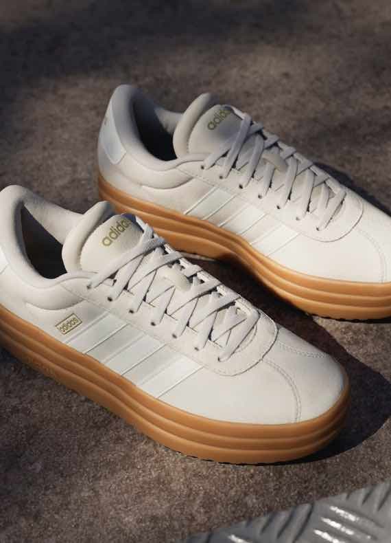 Adidas Sneaker in hellem Ton mit breiter, kontrastfarbener Sohle, seitlichen Streifen und Schnürung auf grauem Untergrund