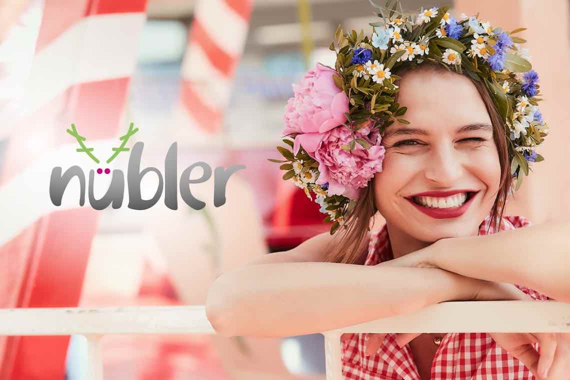 nübler Logo links, rechts Person in kariertem Oberteil mit großem Blumenkranz lehnt an weißem Geländer