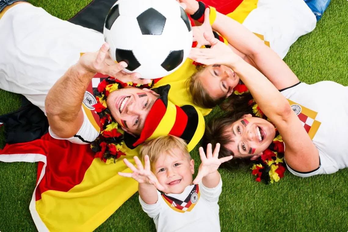 Familie in Deutschland-Fanoutfits liegt auf Rasen und greift gemeinsam nach einem Fußball