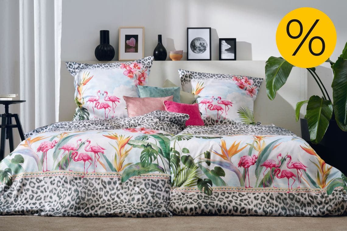 Bett mit bunter Flamingo-Bettwäsche und Leopardenmuster, viele Kissen, gelbes Prozentzeichen für Rabatt-Angebot
