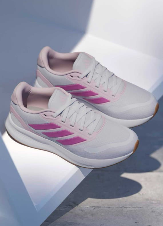 Weiße Sneaker mit rosa Streifen liegen über Kreuz auf heller Kante, Sohlen nach außen sichtbar
