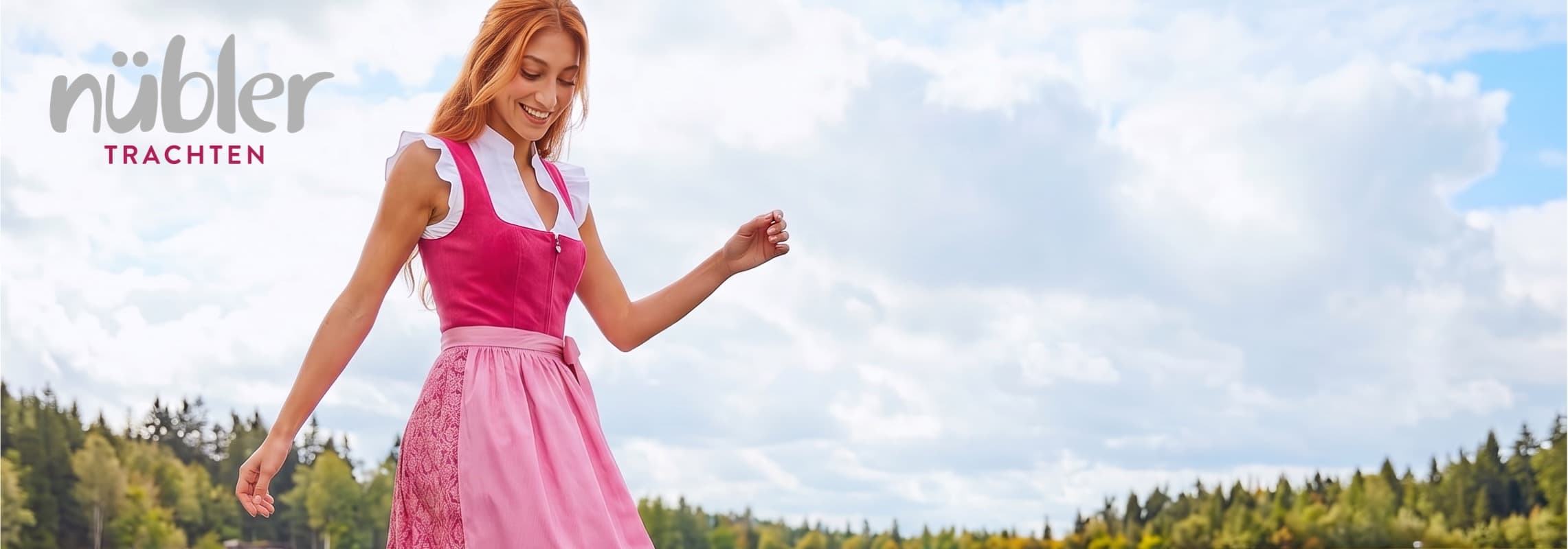 nübler Trachten – Frau im rosa Dirndl steht im Freien vor bewölktem Himmel und Wald im Hintergrund