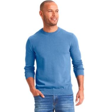 Mann mit kurzem Haar und Bart trägt blauen Pullover und Jeans und steht mit Händen in den Hosentaschen