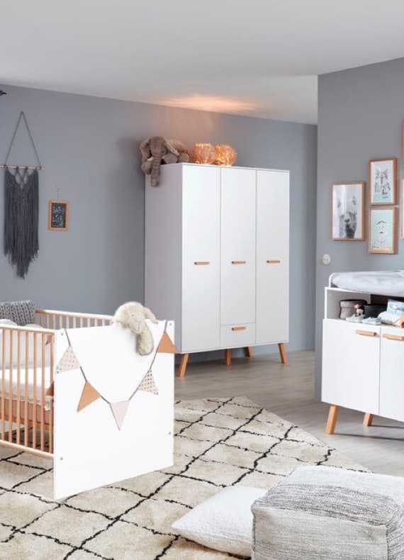 Babyzimmer mit Gitterbett, Wickelkommode und Kleiderschrank in Weiß vor grauer Wand mit Bildern und Deko