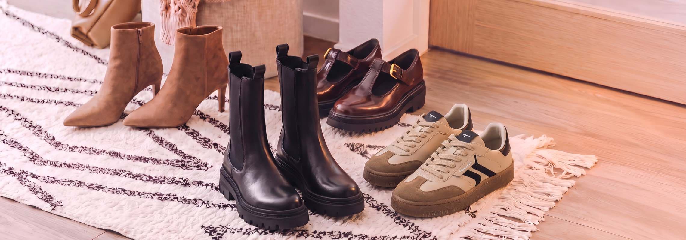 Vier Paar Damenschuhe auf Teppich: Stiefeletten, schwarze Chelsea-Boots, braune Loafer und beige Sneaker nebeneinander
