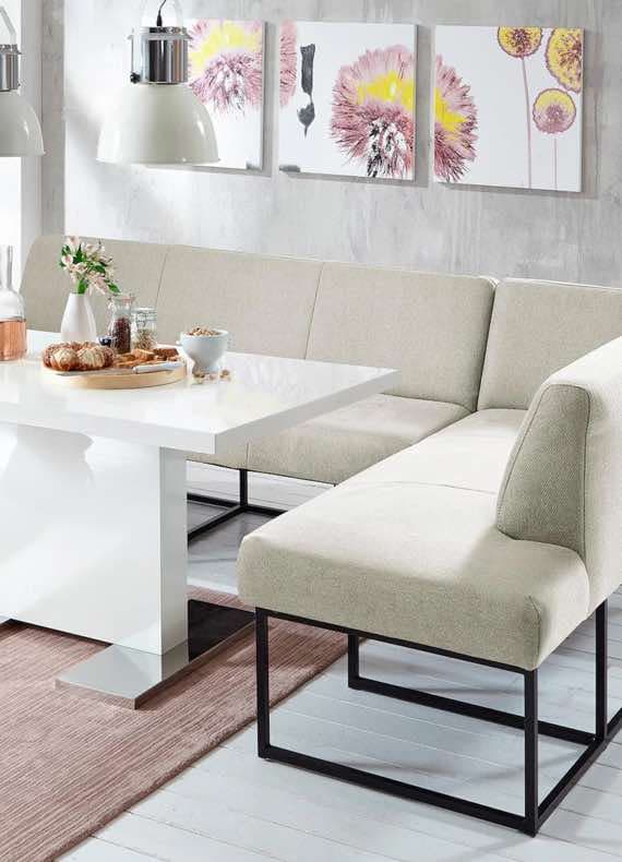 Eckbankgruppe mit weißem Tisch, beige Polsterung, dekoriert mit Frühstück und Blumenbildern an der Wand.